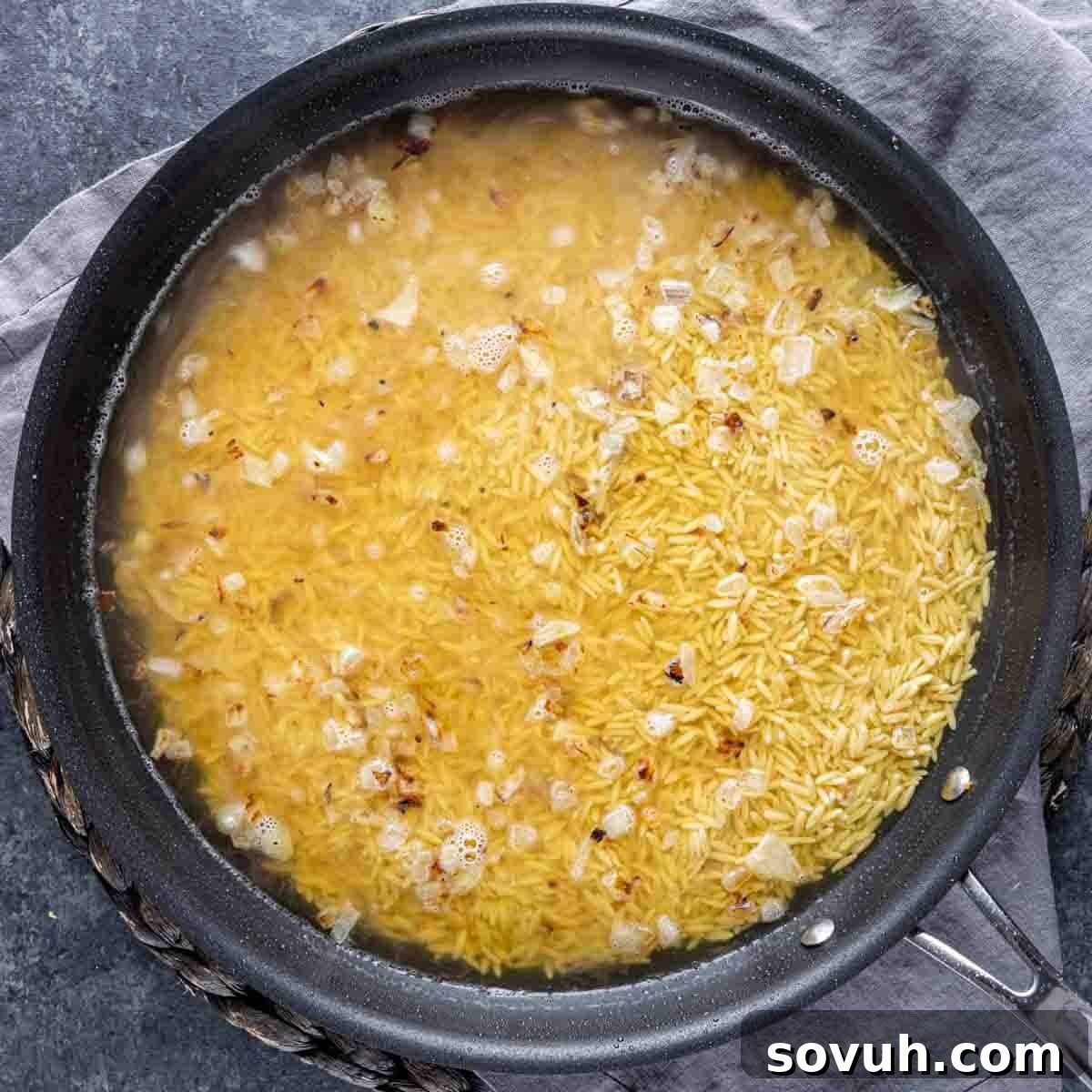 A pot of simmering Parmesan Chicken Orzo with diced onions and garlic, creating a fragrant base for the pasta.