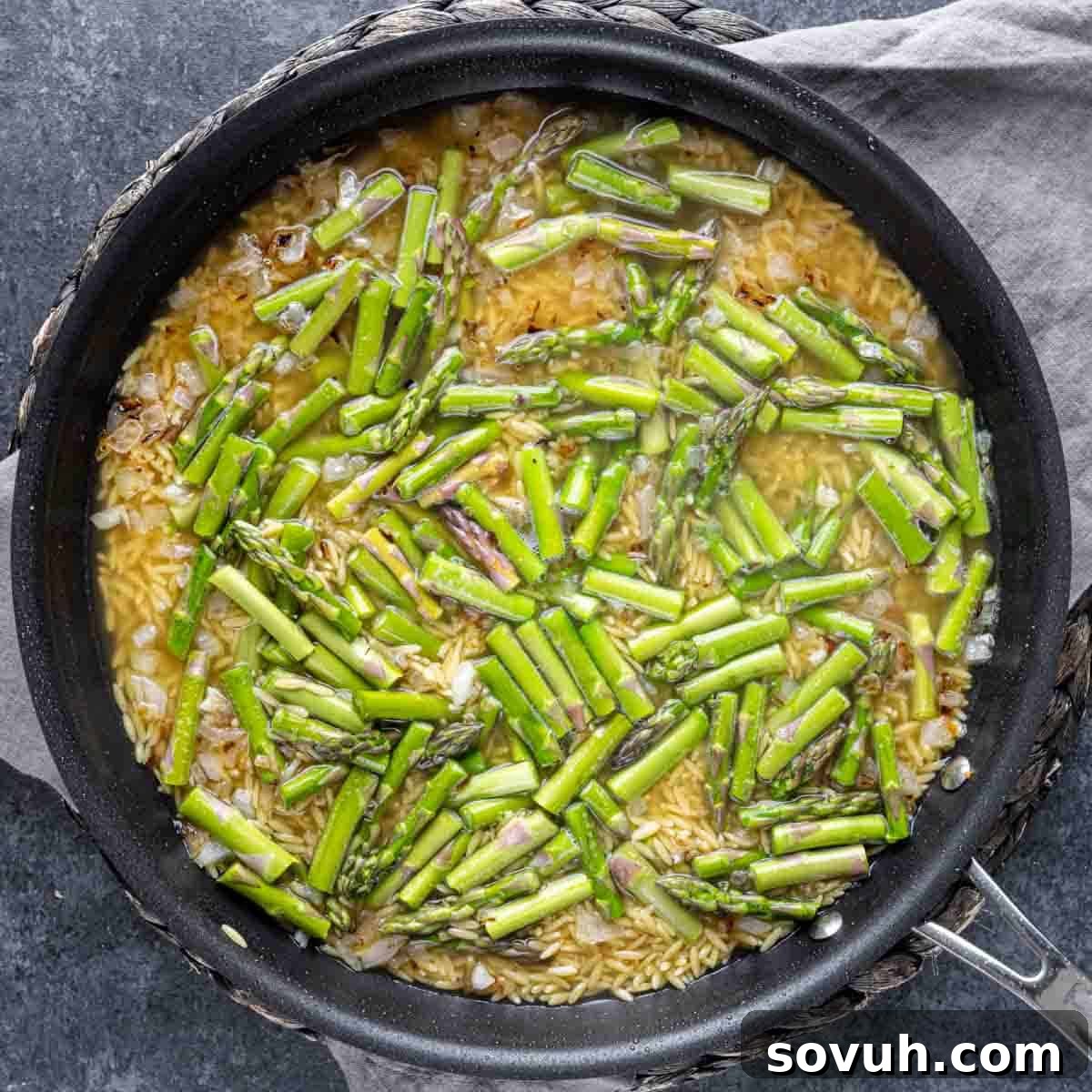 Parmesan Chicken Orzo cooking in a pan, with the orzo absorbing the liquid and asparagus spears nestled among the pasta.