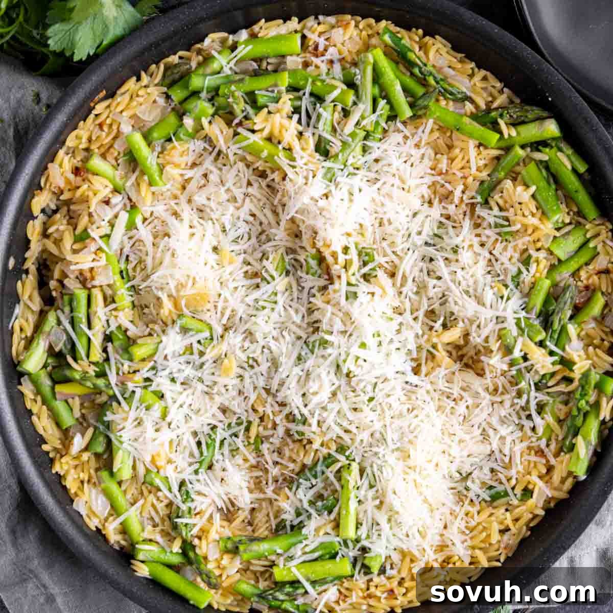 A skillet of Parmesan Chicken Orzo with asparagus and grated cheese on top, ready for final stirring.