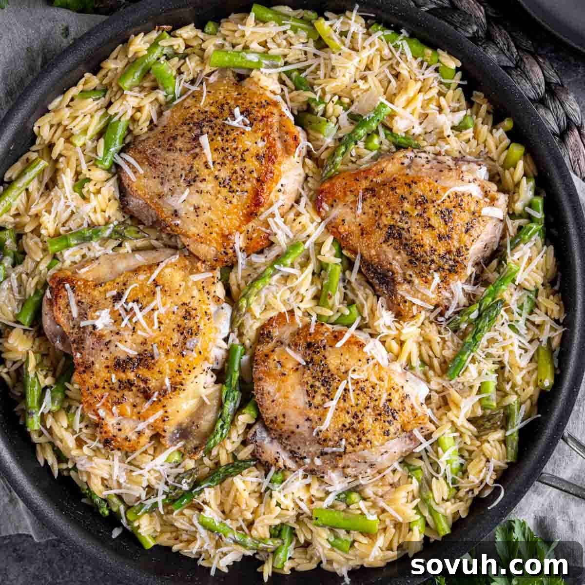 Parmesan Chicken Orzo served over a bed of creamy orzo pasta and asparagus, garnished with extra grated cheese and fresh lemon wedges, showcasing a complete and appetizing meal.