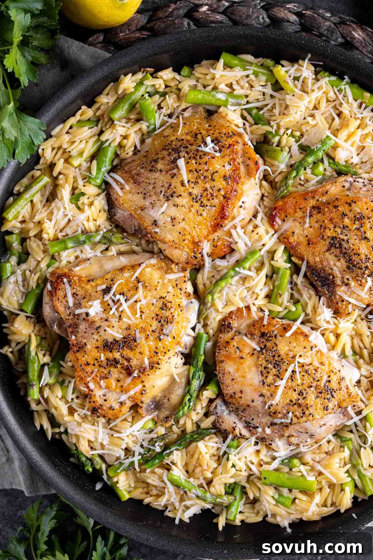 Four servings of Parmesan Chicken Orzo with asparagus and golden-brown chicken thighs, presented beautifully in a black skillet, ready to be enjoyed.
