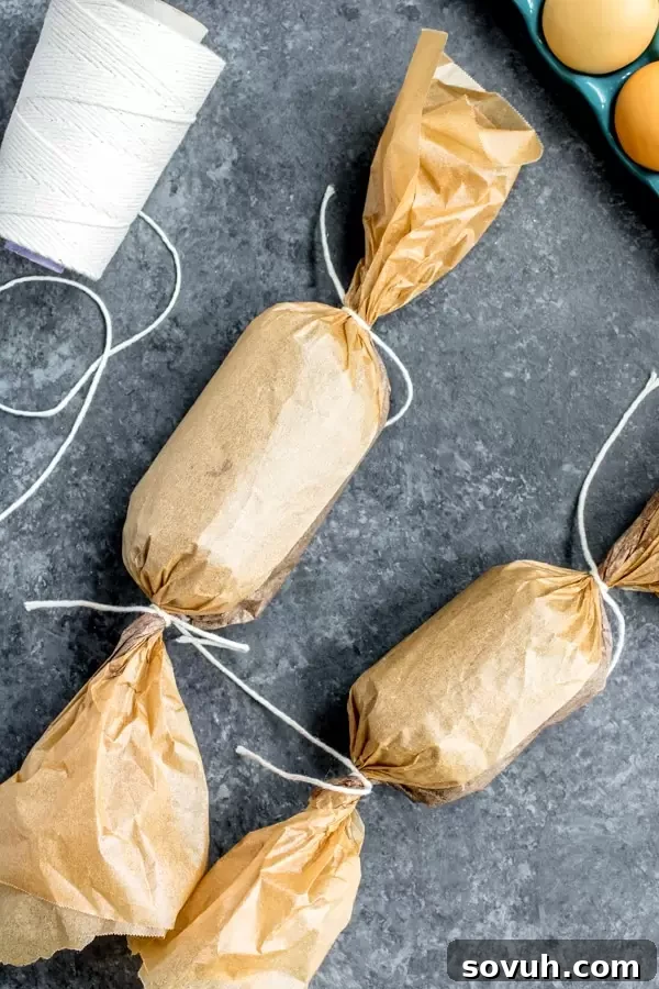 Two rolls of Chocolate Salami, tightly wrapped in parchment paper and tied, chilling in the refrigerator.