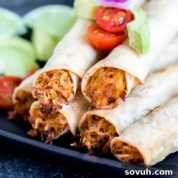 Chicken Taquitos stacked on plate, golden brown and crispy, with fresh garnishes.