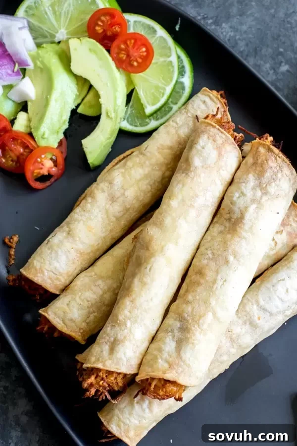 Close-up of a plate of Baked Chicken Taquitos with a side of sliced avocado.