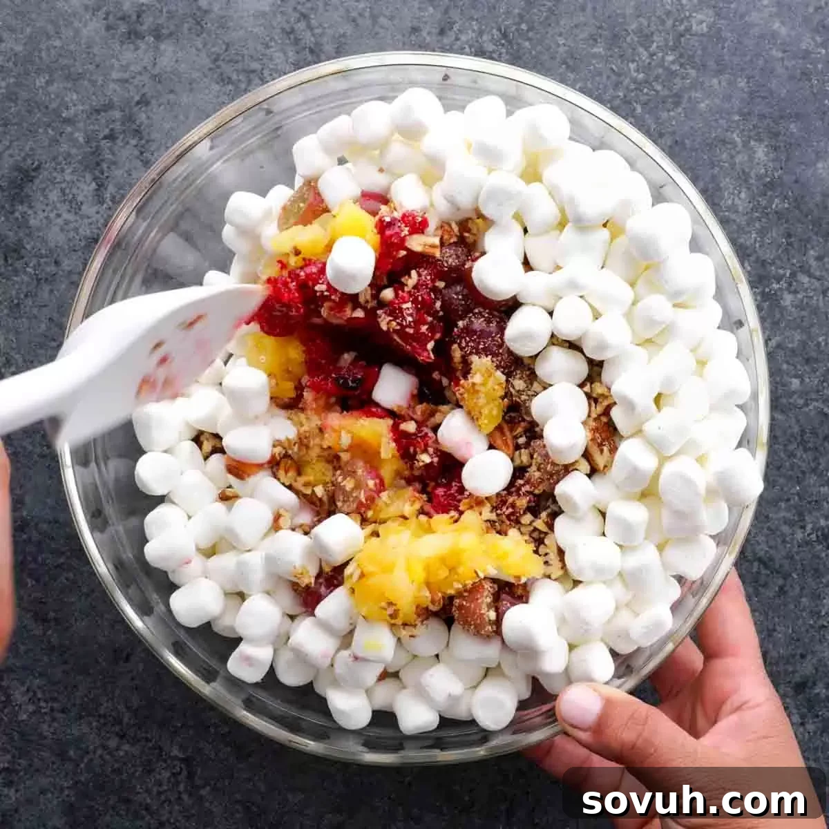 A person gently scooping mini marshmallows into a large bowl with other cranberry fluff ingredients.