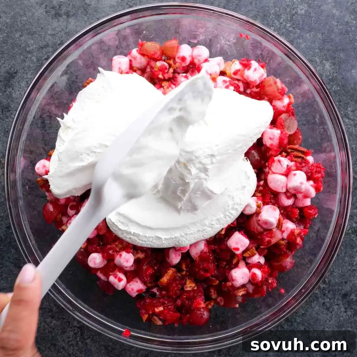 A person gently folding Cool Whip into the cranberry mixture in a large bowl, creating the creamy Cranberry Fluff Salad.