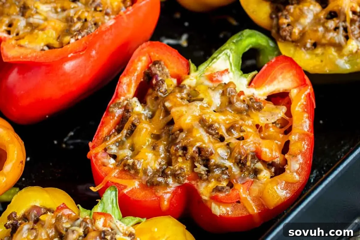 Close-up of baked red bell peppers stuffed with ground meat and topped with melted cheese on a baking tray.