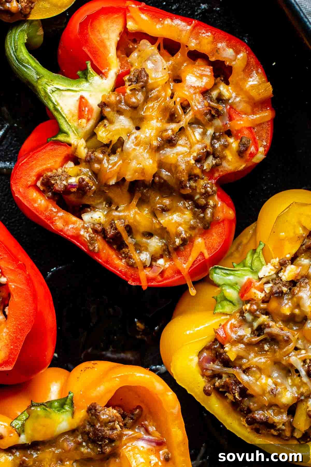 Close-up of red and yellow bell peppers stuffed with ground meat and shredded cheese, baked until cheese is melted.