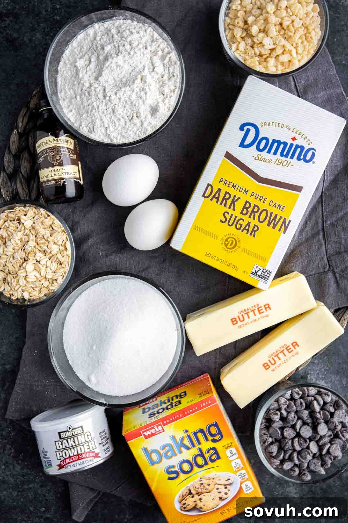 Assortment of fresh ingredients for Ranger Cookies laid out, including butter, sugars, eggs, flour, oats, Rice Krispies, and chocolate chips