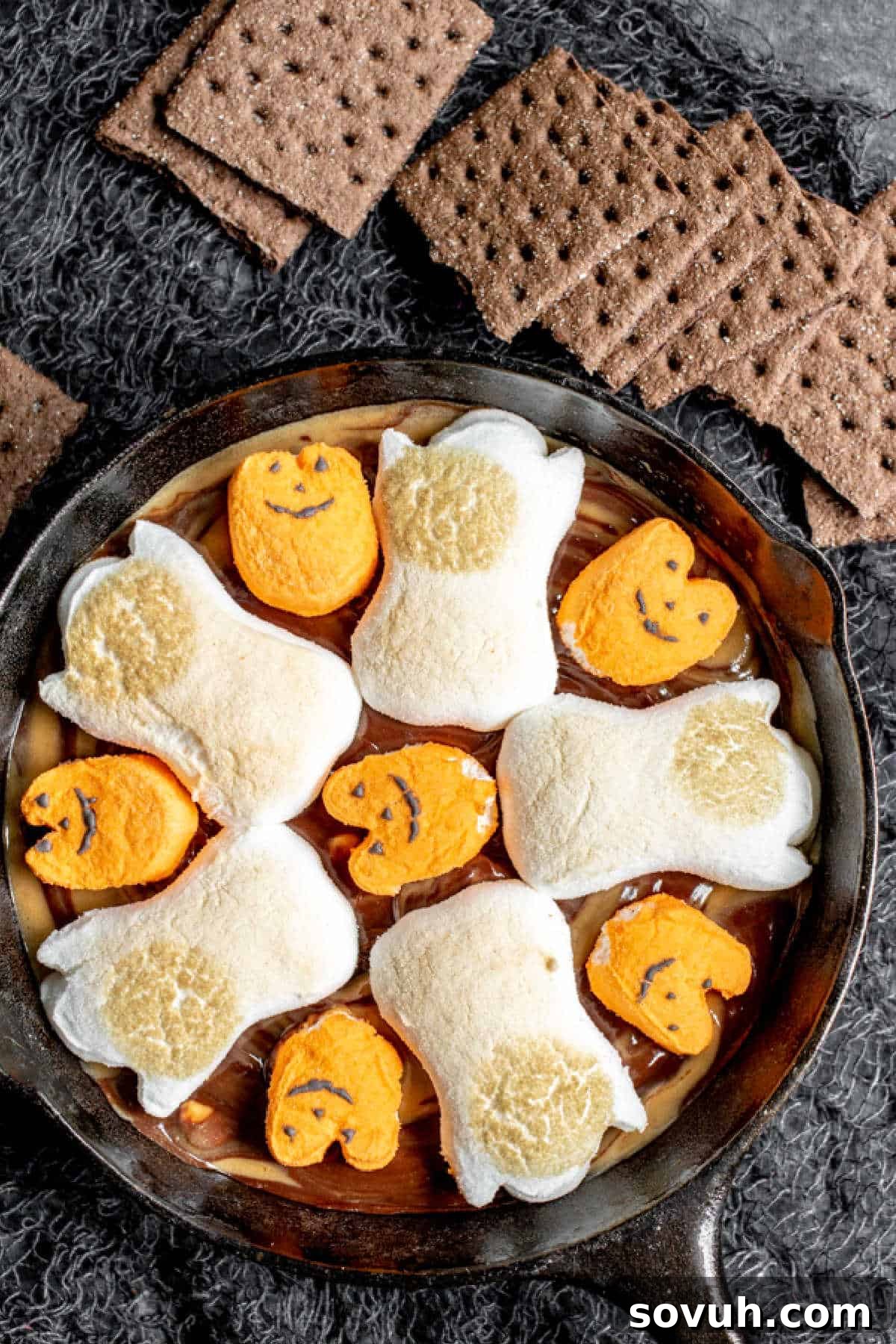 A warm skillet of Halloween S'mores Dip served with chocolate graham crackers, highlighting the melted chocolate, peanut butter, and toasted Halloween marshmallows.