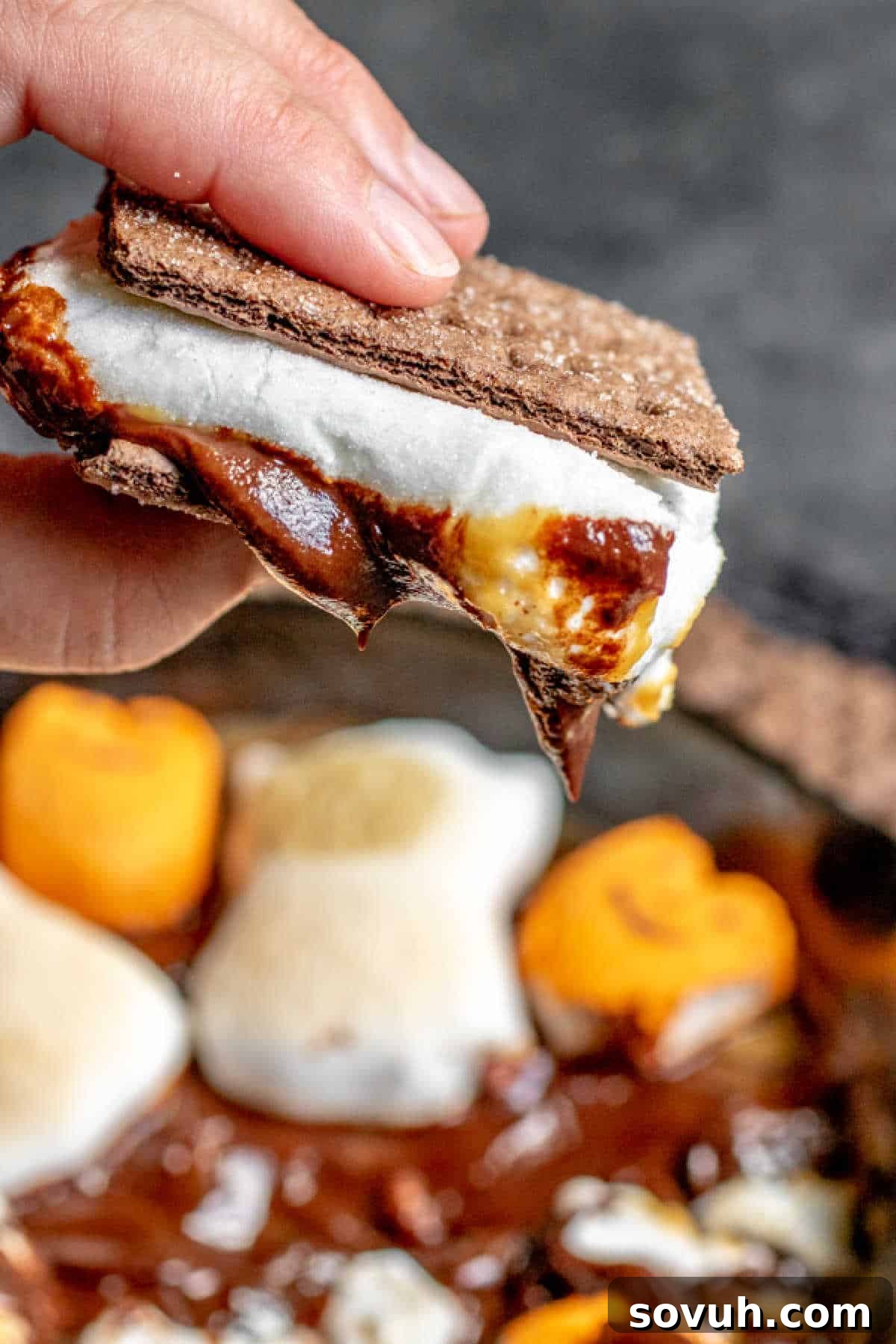 A person holding a s'more creation made by dipping a graham cracker into the Halloween S'mores Dip, with the toasted Peeps visible.