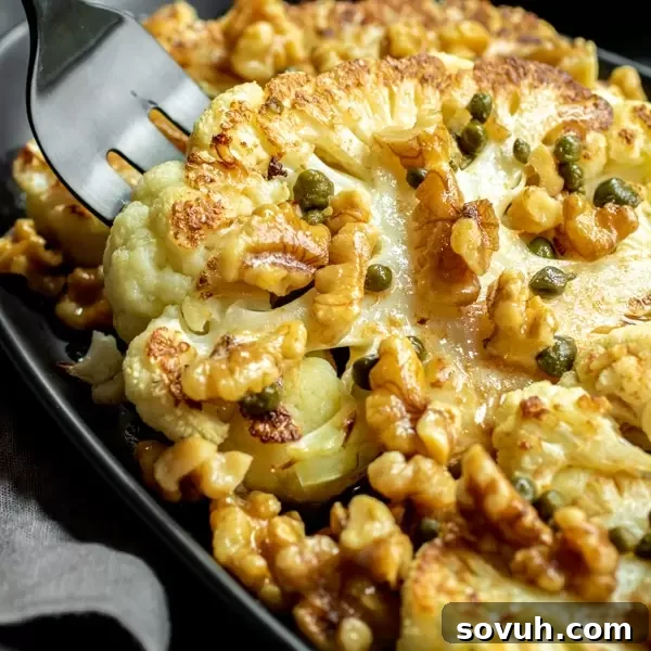 A fork lifting a piece of roasted cauliflower steaks with toasted walnuts, capers, and brown butter. A low carb, keto, and vegetarian dinner or side dish.
