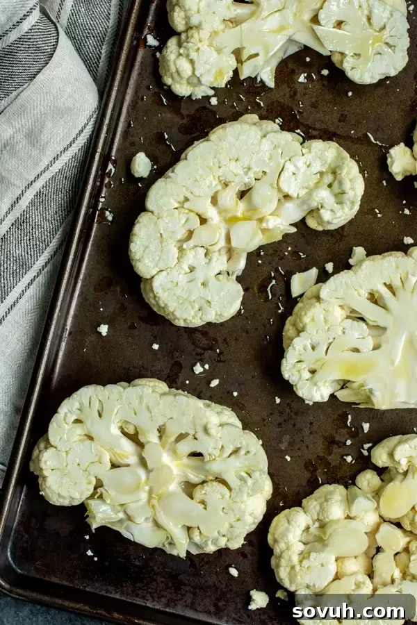 A raw head of cauliflower sits on a baking sheet, ready to be sliced into steaks and roasted.