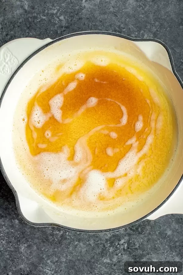 A white skillet holds a pool of golden-brown butter, illustrating the final stage of the browning process.