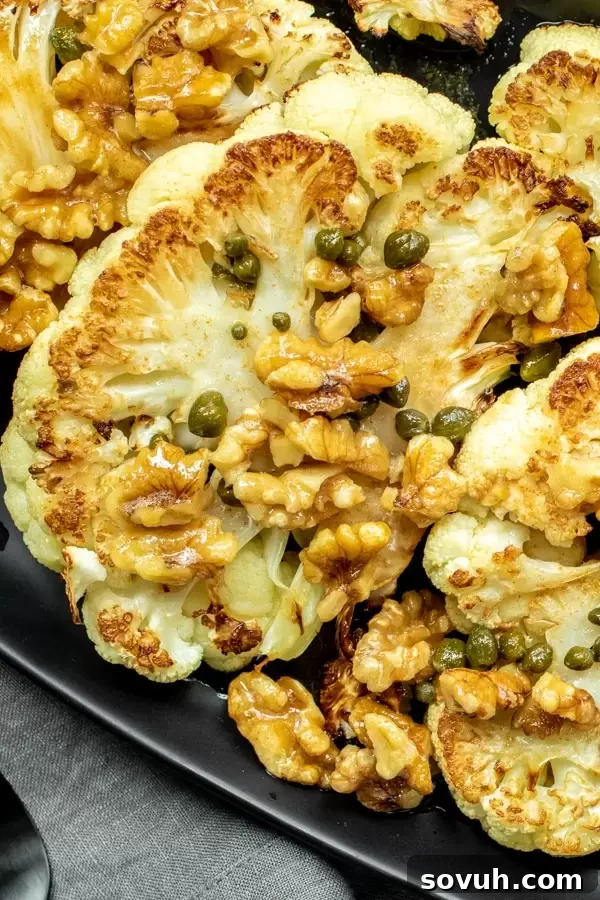 Close-up of roasted cauliflower steaks generously topped with capers, toasted walnuts, and brown butter, ready to be served.