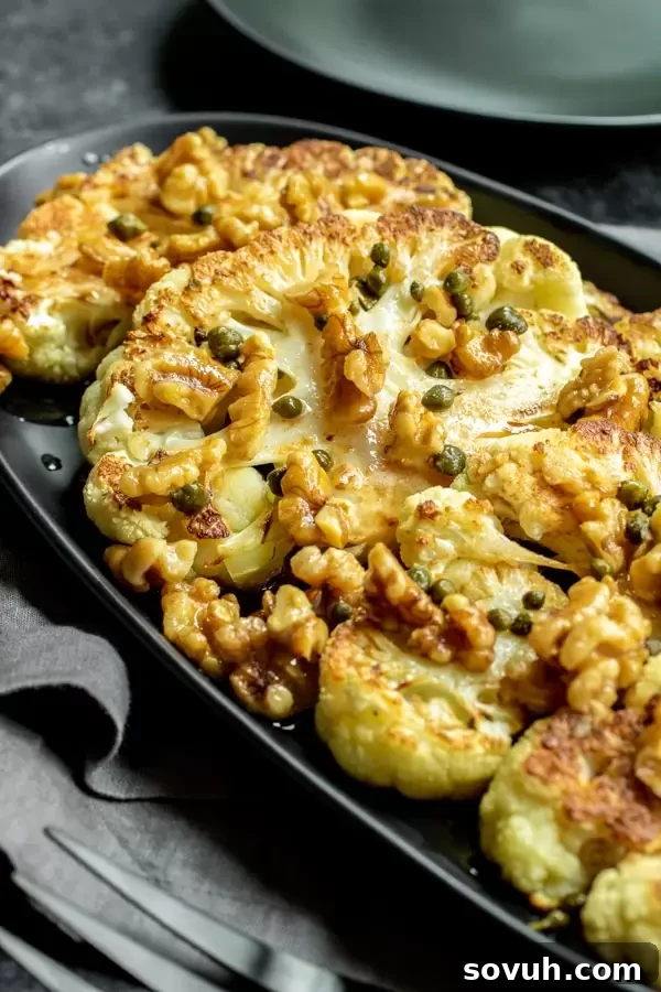 Several perfectly roasted cauliflower steaks with brown butter, capers, and walnuts, artfully fanned out on a black plate, ready to be served.