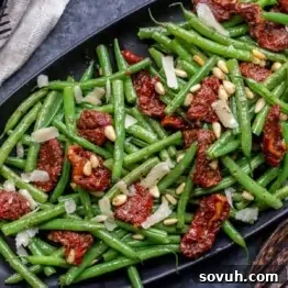 A plate of green beans mixed with sun-dried tomatoes, pine nuts, and shavings of Parmesan cheese.