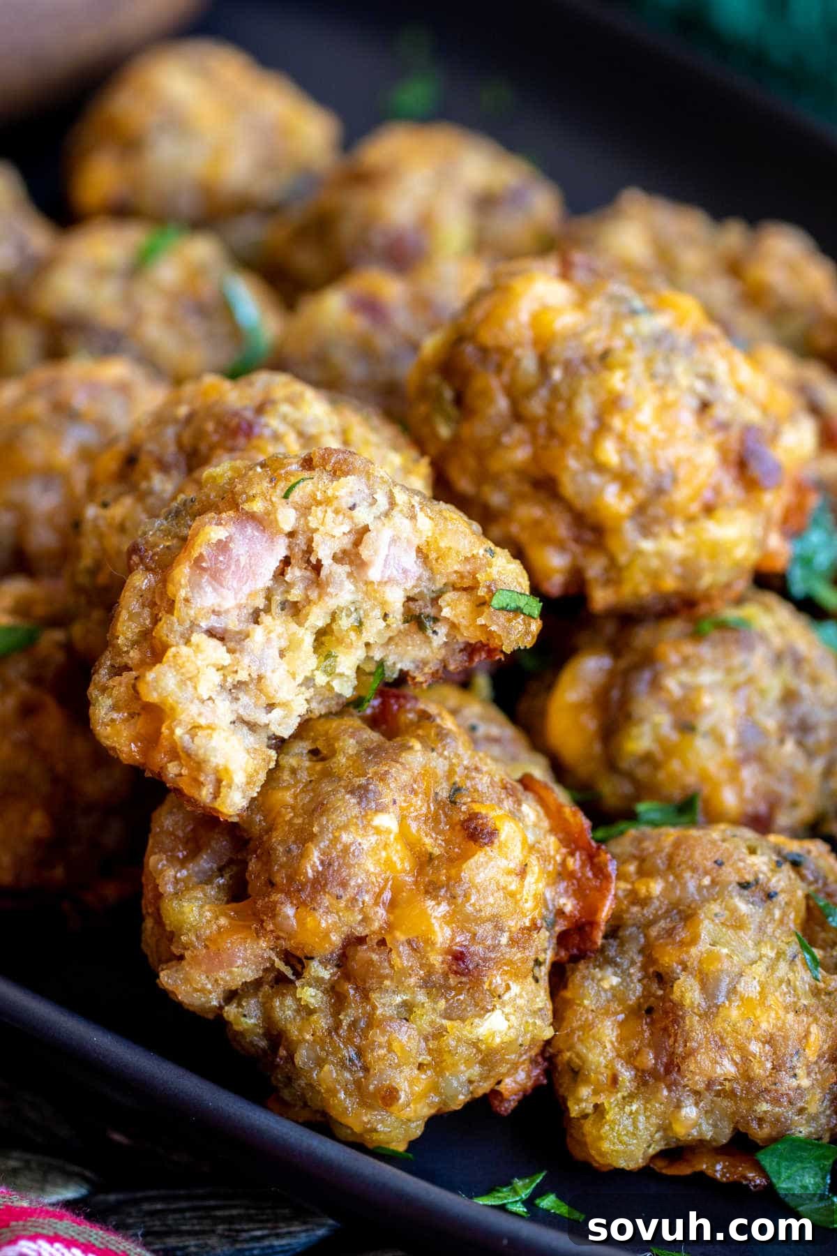 A black plate piled high with golden-brown Sausage Stuffing Balls, garnished with a sprig of fresh rosemary, inviting guests to enjoy this delicious holiday appetizer.