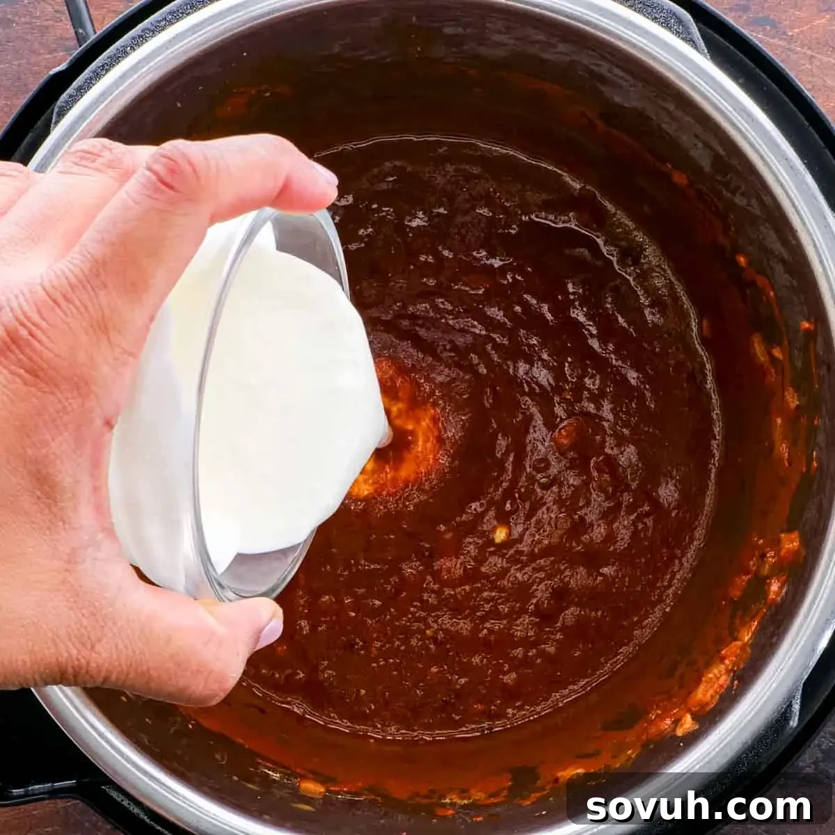 A person pouring heavy cream into the Instant Pot, preparing to blend the rich butter chicken sauce.