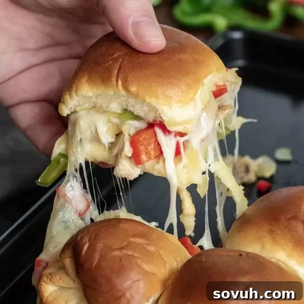 A delicious chicken cheesesteak slider with provolone cheese oozing out, surrounded by other sliders on a tray.