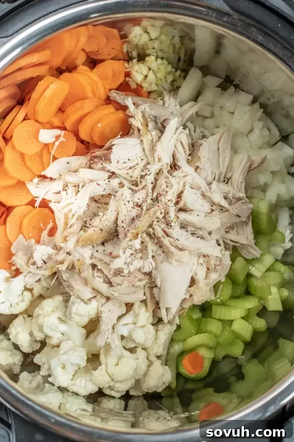 Fresh ingredients laid out for Instant Pot Creamy Chicken Soup, including carrots, celery, onion, cauliflower, garlic, chicken, and broth.