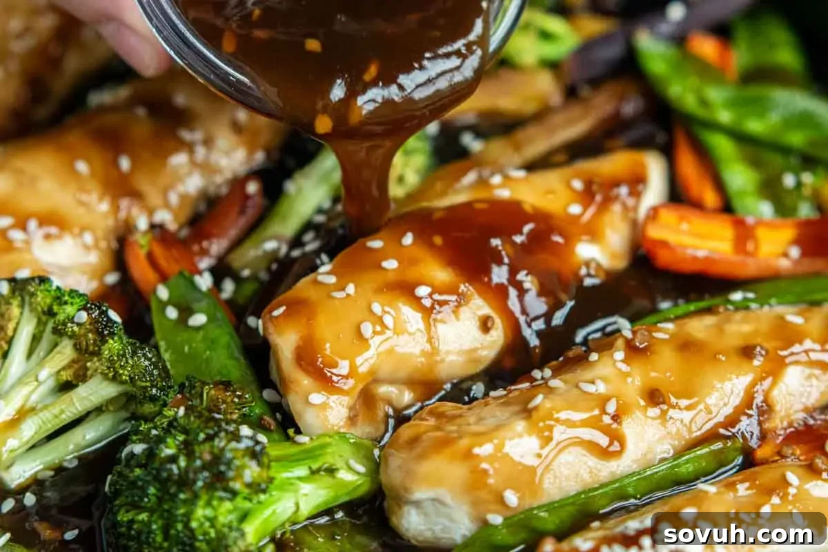 Honey garlic sauce being poured over chicken pieces with broccoli, carrots, and snap peas, garnished with sesame seeds, creating a vibrant, mouth-watering scene.