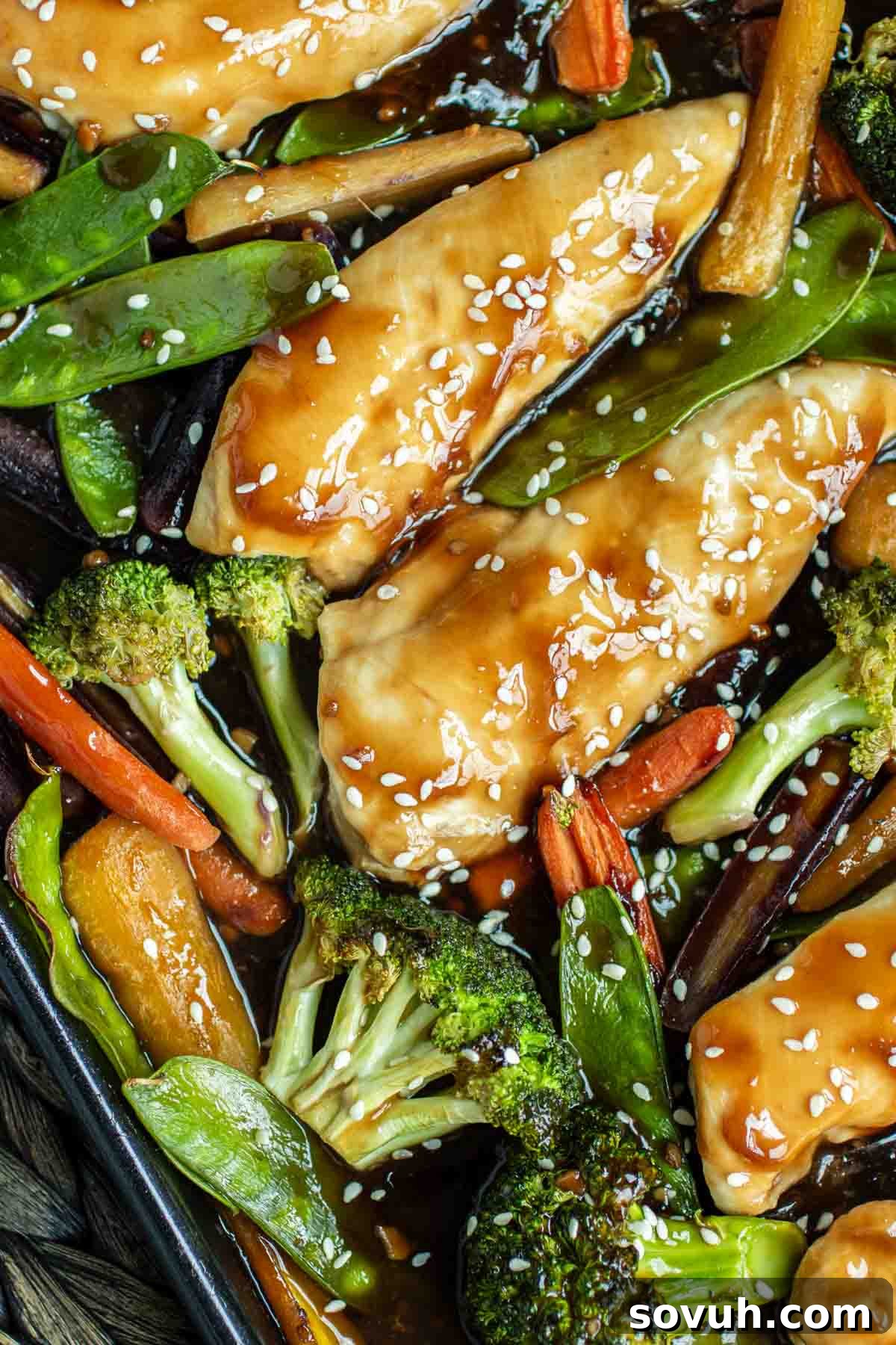 A close-up of glazed chicken with tender broccoli florets, vibrant carrots, and fresh snow peas, generously coated in a shimmering honey garlic sauce and sprinkled with sesame seeds.