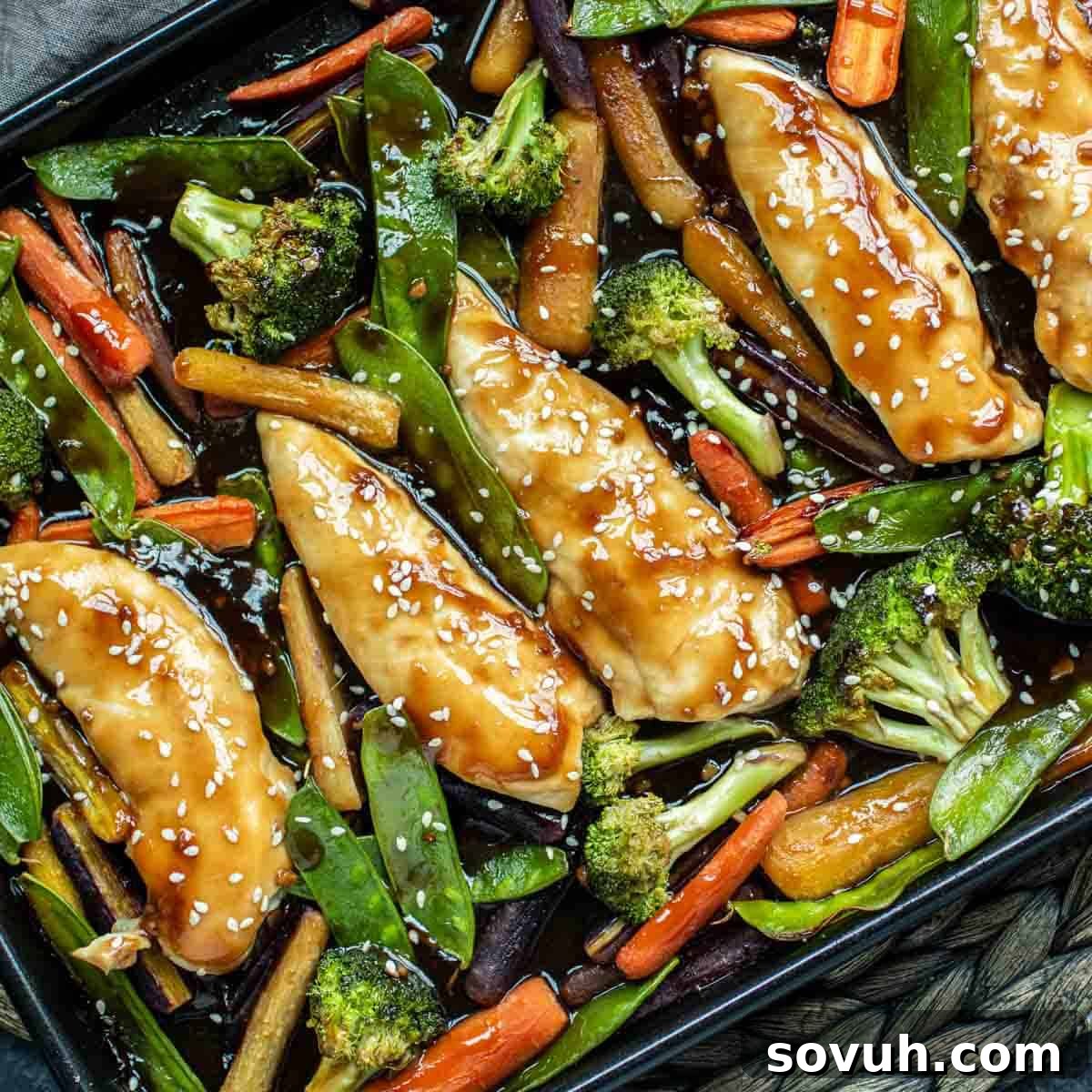 Glazed chicken breasts with sesame seeds on a baking tray, surrounded by vibrant broccoli, crisp snap peas, and tender carrots, all ready to be served.