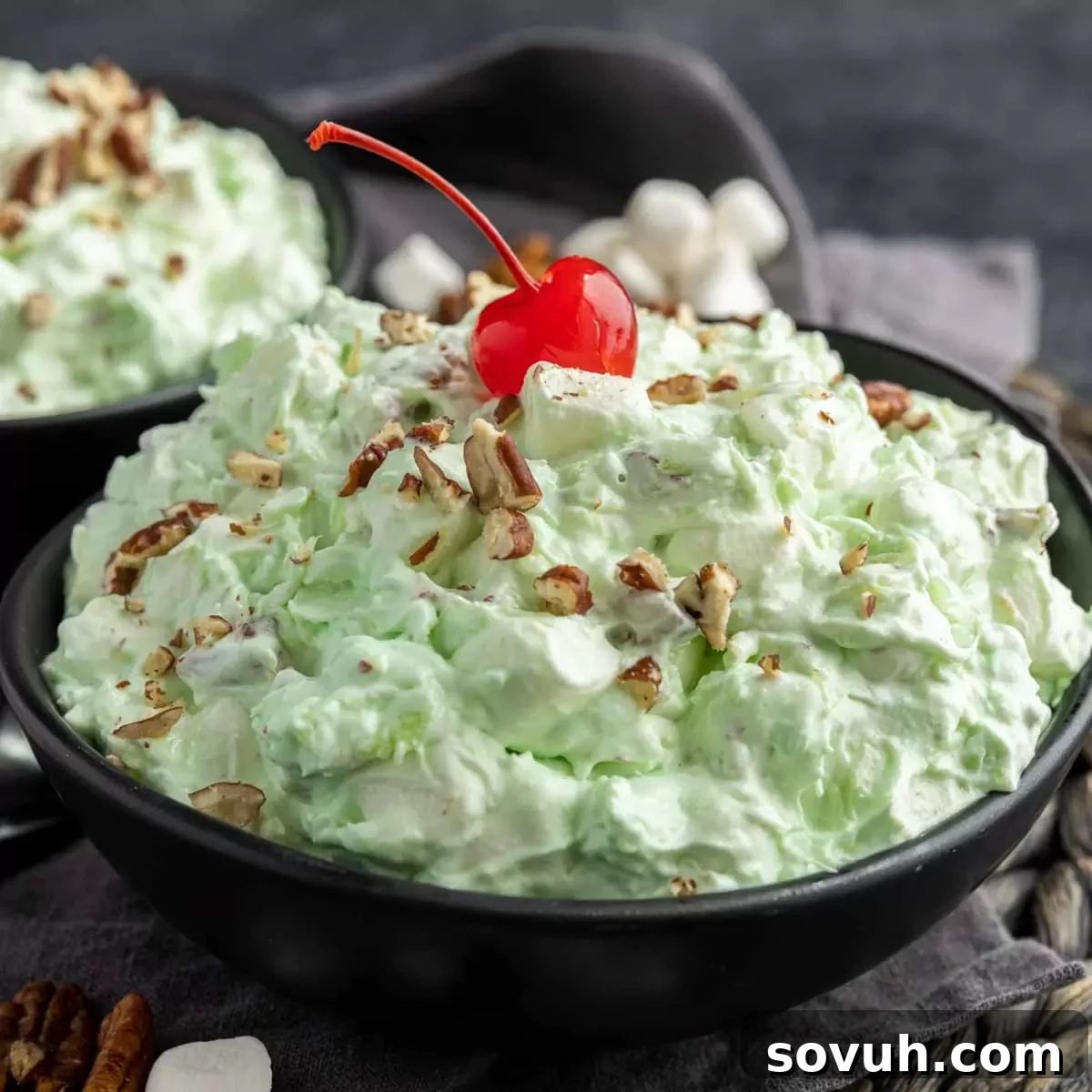 A bowl of vibrant green Watergate Salad, topped with a cherry and chopped pecans, ready to be served at a festive occasion.