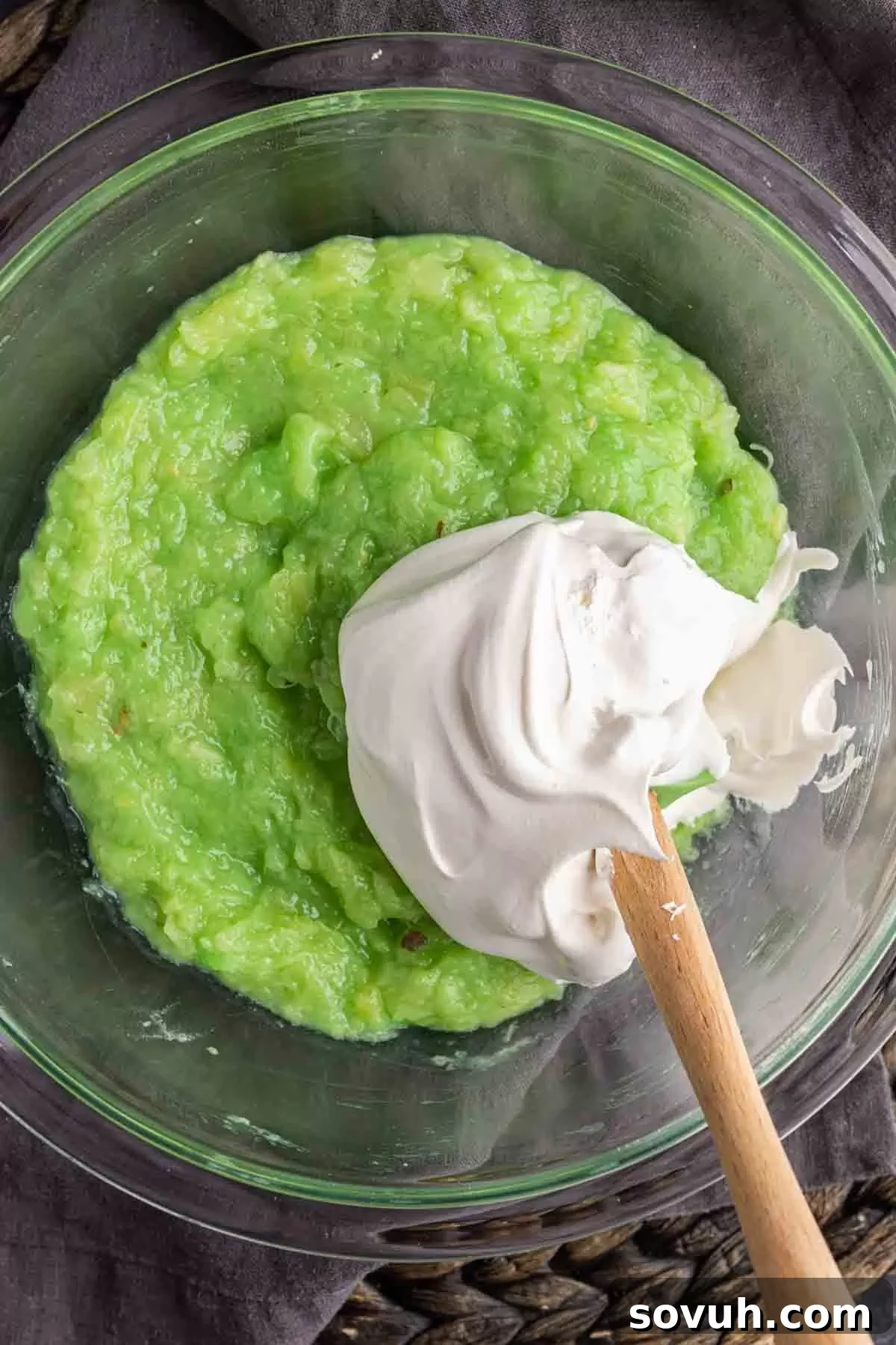 A close-up of Watergate Salad being mixed with Cool Whip, showcasing its creamy, fluffy texture and signature green color.