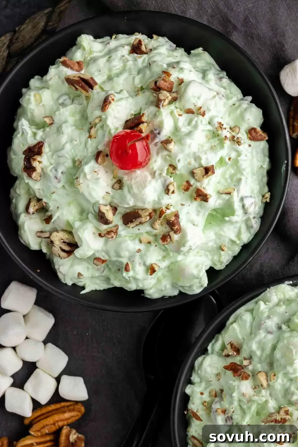 A beautifully presented bowl of Watergate Salad, garnished with a sprinkle of chopped pecans and a bright red maraschino cherry on top, ready for a festive table.