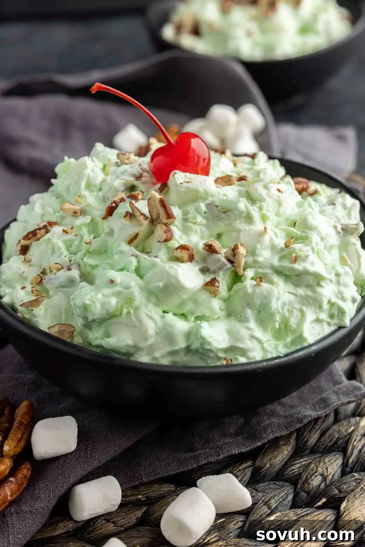 A pristine bowl of Watergate Salad, topped with a single maraschino cherry and a delicate sprinkle of chopped pecans, sitting on a wooden surface.