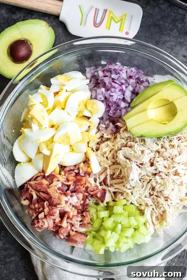 All the fresh ingredients for a creamy avocado chicken salad: shredded chicken, avocado, red onion, celery, hard-boiled eggs, bacon, and mayonnaise.