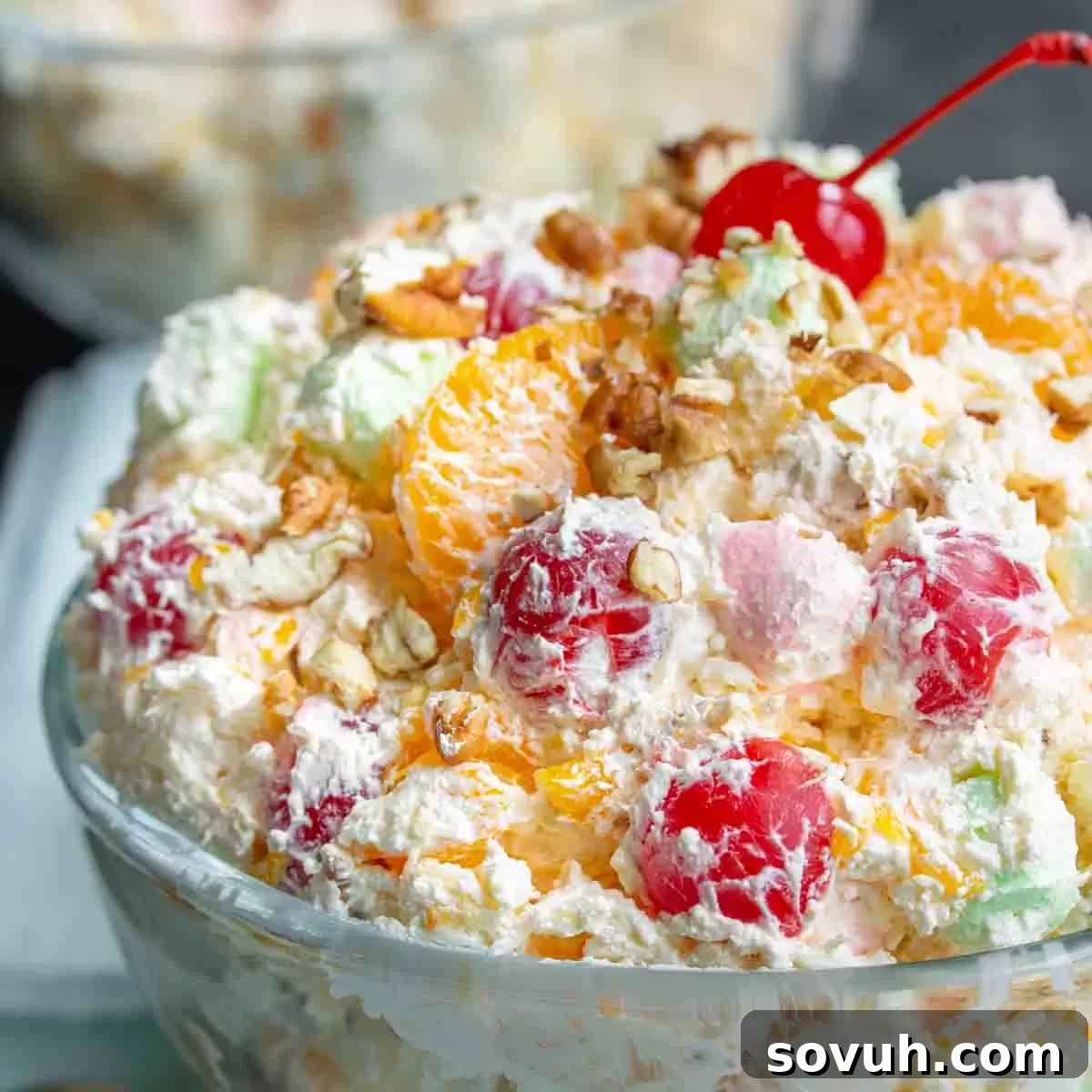 A side shot of a beautiful, fluffy Ambrosia Salad in a clear glass bowl, showcasing its colorful ingredients like mandarin oranges, cherries, and marshmallows, perfect for a Southern dessert spread.