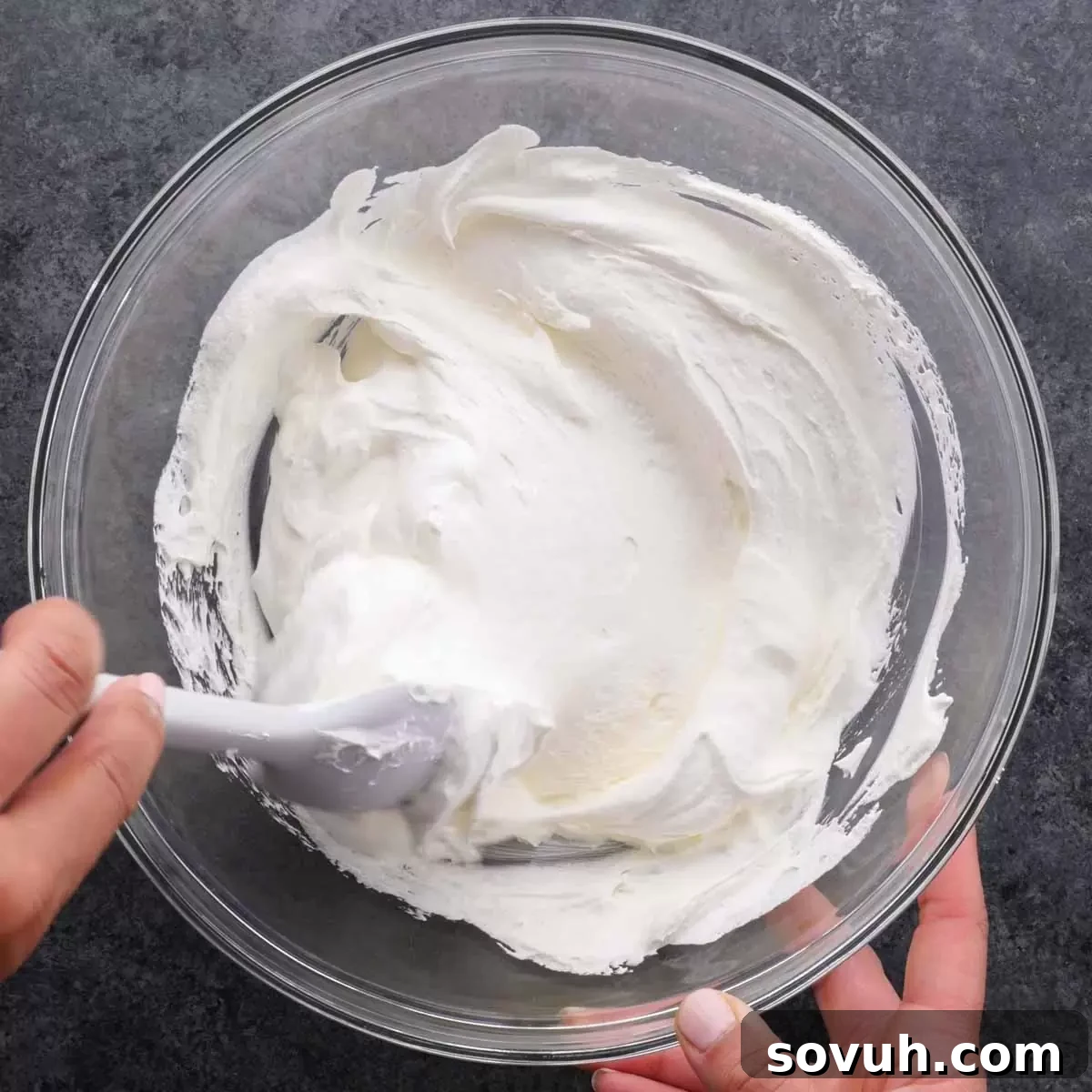 Step-by-step image of Cool Whip and sour cream being stirred together in a large mixing bowl until fully combined and smooth.