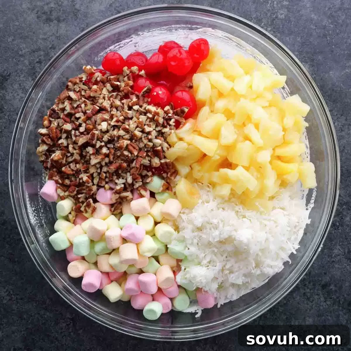 Step-by-step image showing fruit-flavored marshmallows, shredded coconut, pineapple tidbits, maraschino cherries, and pecans being folded into the creamy base.