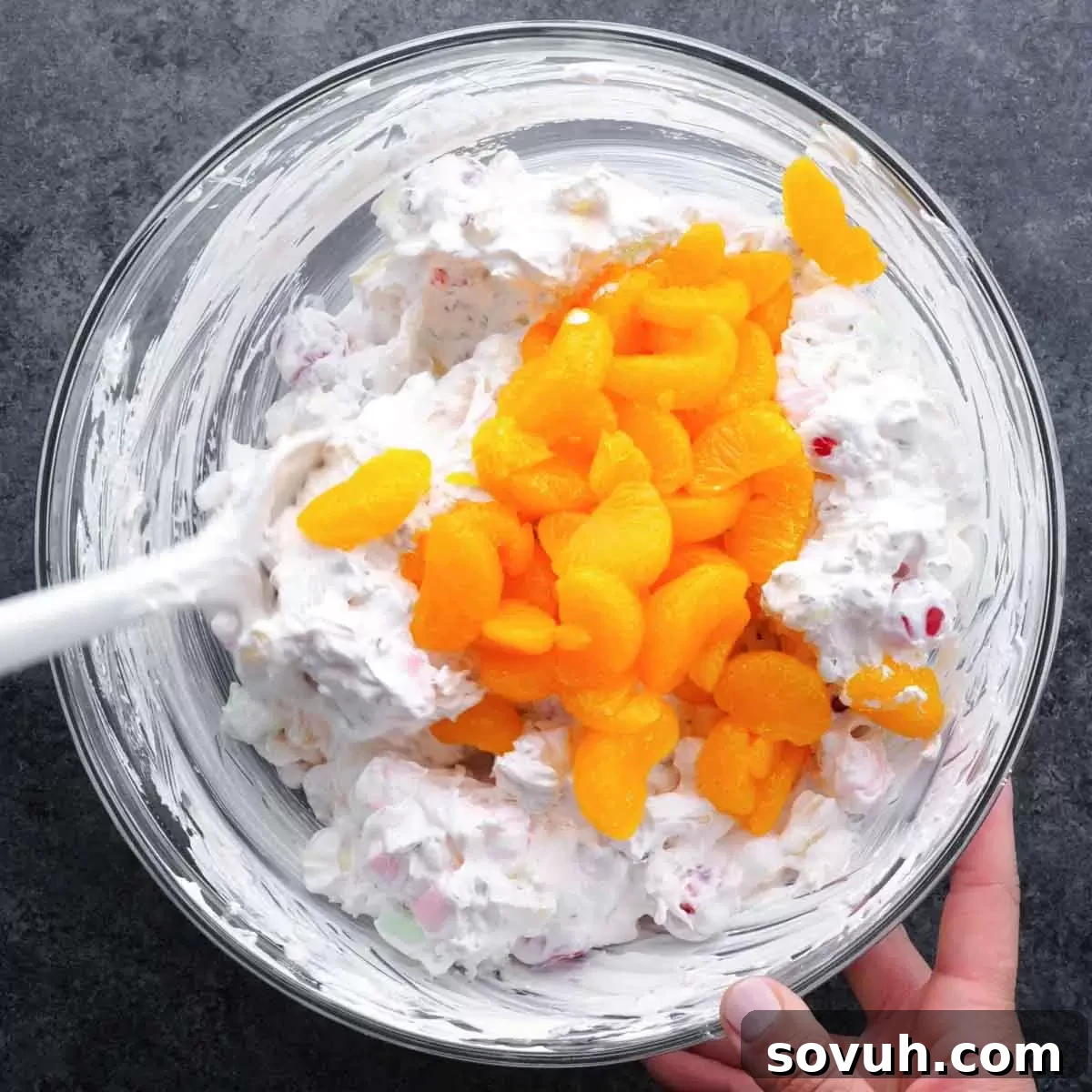 Step-by-step image of mandarin orange segments being carefully added last and gently folded into the Ambrosia Salad mixture to prevent breaking them.