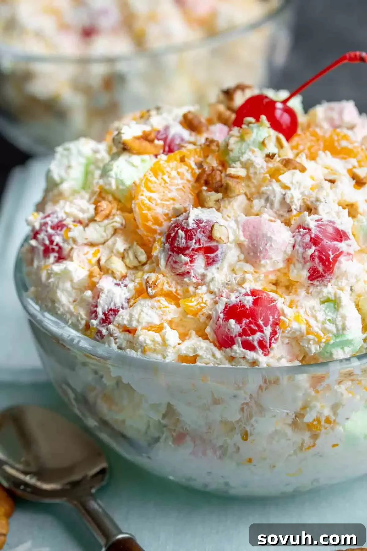 A large, clear glass bowl filled with fluffy, colorful marshmallow fruit salad, Ambrosia Salad, ready to be served, highlighting its inviting presentation.