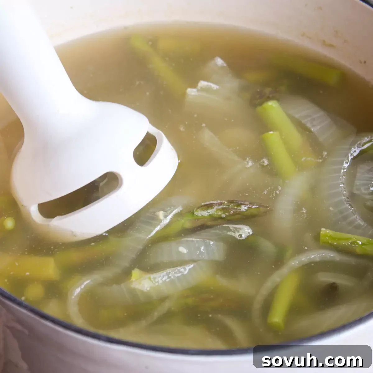 A step-by-step image showing how to puree creamy asparagus soup in a pot using an immersion blender.