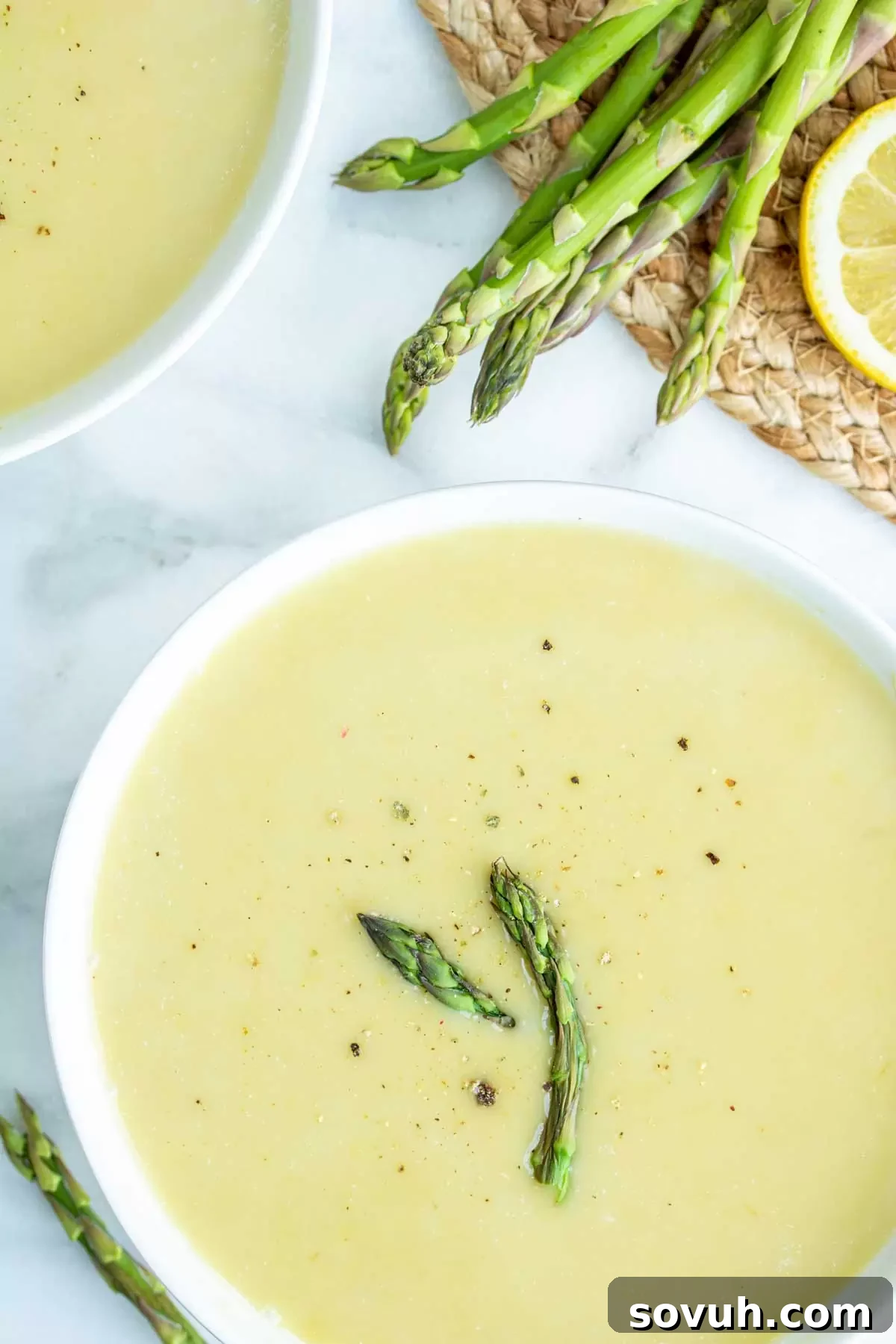 A charming close-up of a bowl of creamy asparagus soup, garnished with a sprig of fresh thyme, placed on a light marble countertop.