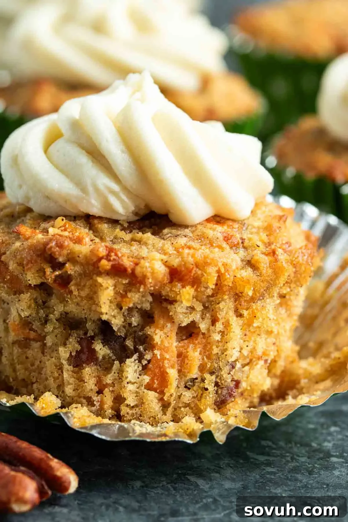 A close-up of a beautifully frosted Keto Carrot Cake Cupcake with cream cheese frosting and a sprinkle of pecans on a rustic dark surface.