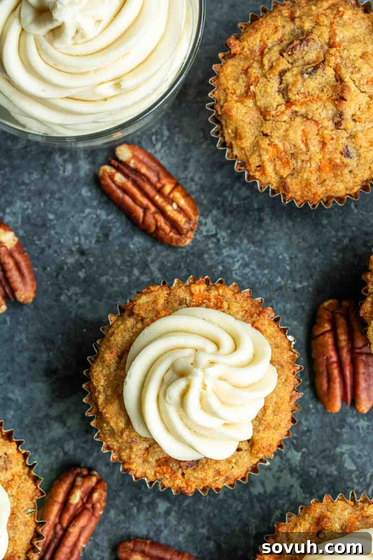Close-up of a Keto Carrot Cake Cupcake featuring a generous swirl of cream cheese frosting and a sprinkle of pecan toppings, set against a rich, dark surface.