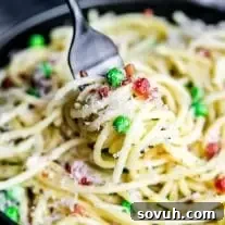 A fork twirled in creamy pasta carbonara, showing the rich sauce and crispy pork bits.