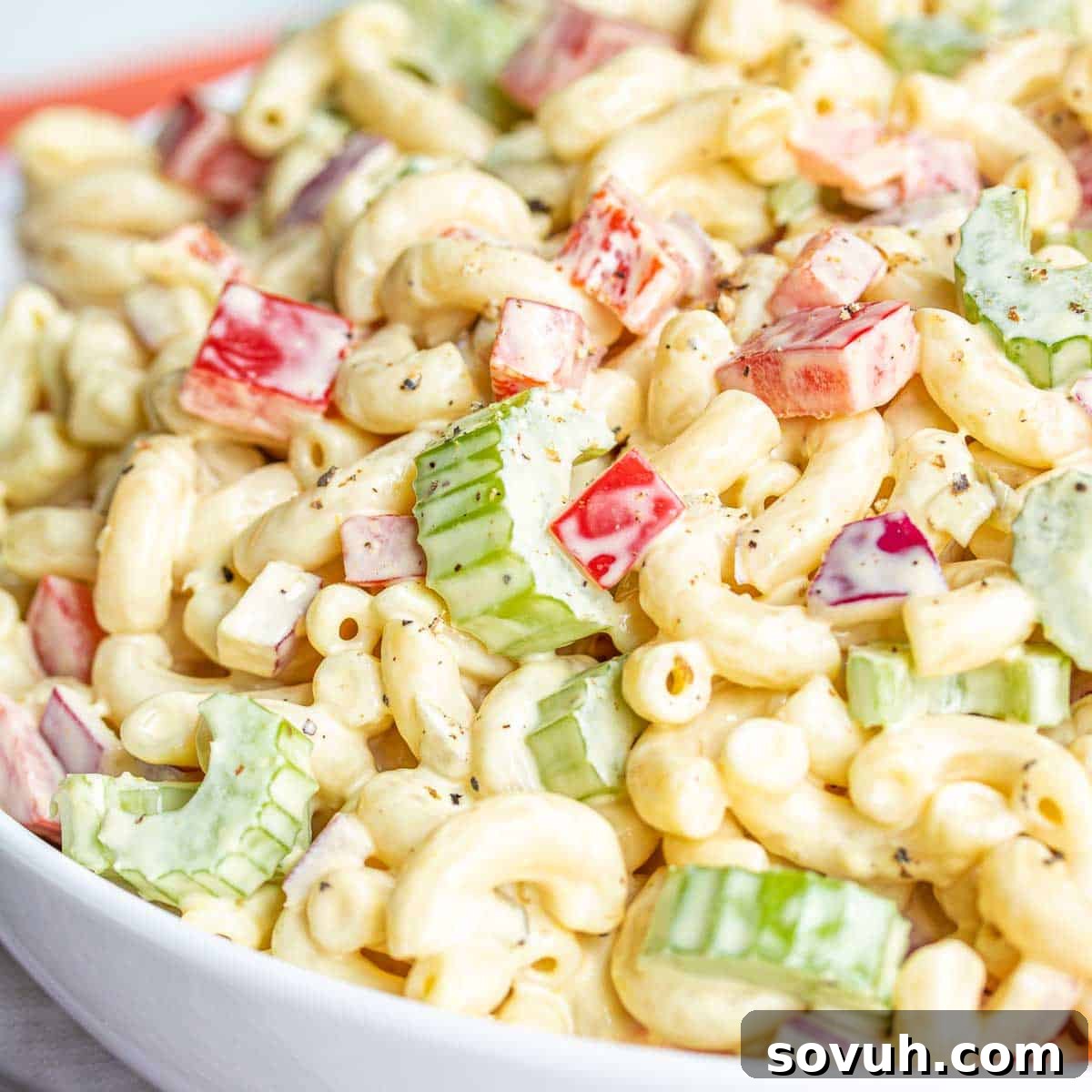 A vibrant bowl of classic macaroni salad, featuring tender elbow macaroni, crisp red bell peppers, and fresh celery, coated in a creamy, tangy dressing. Perfect for any gathering, from summer barbecues to holiday dinners.