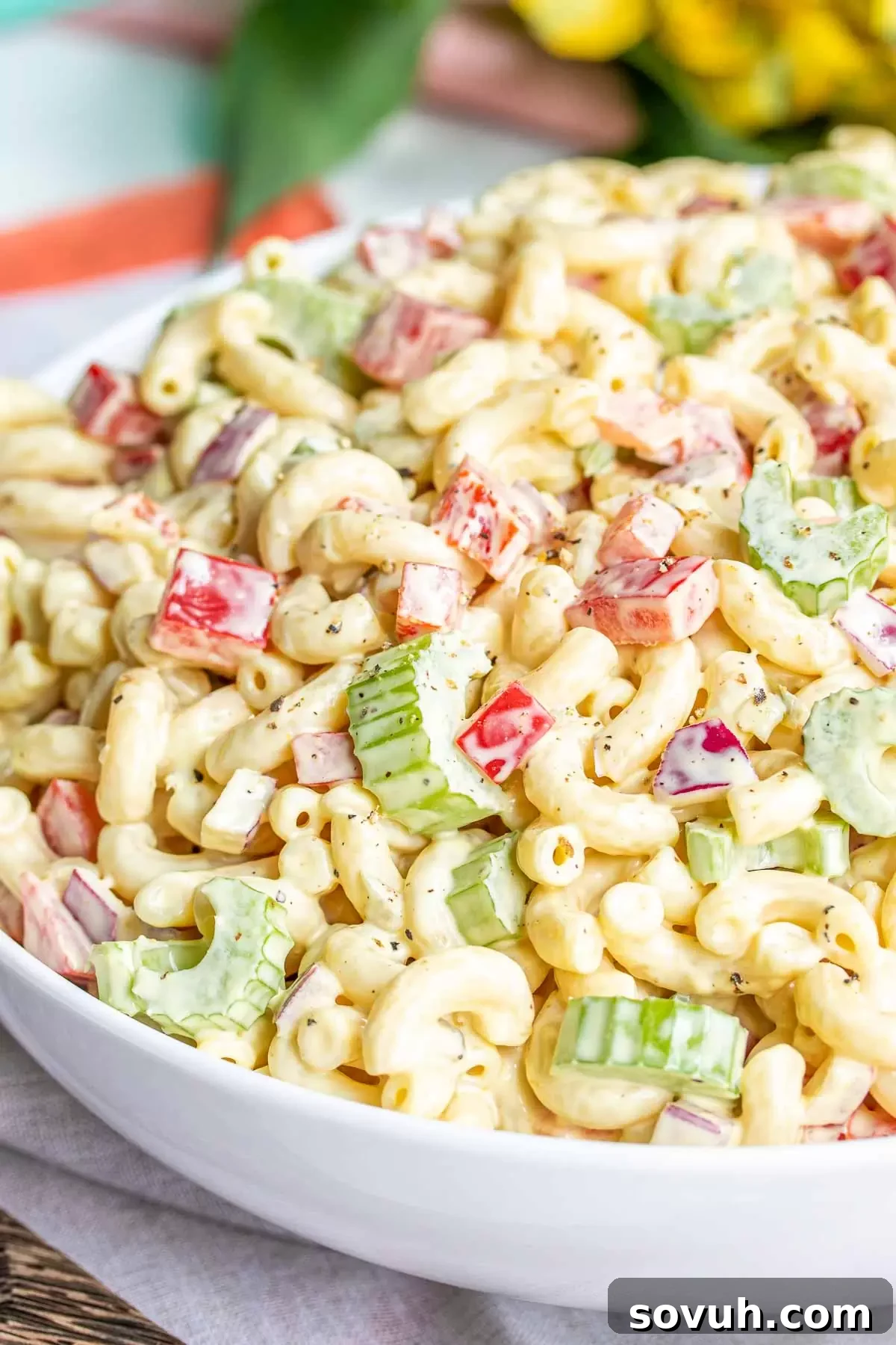 A beautifully presented white bowl overflowing with homemade classic macaroni salad, garnished with fresh parsley, ready to be served. The perfect make-ahead dish.