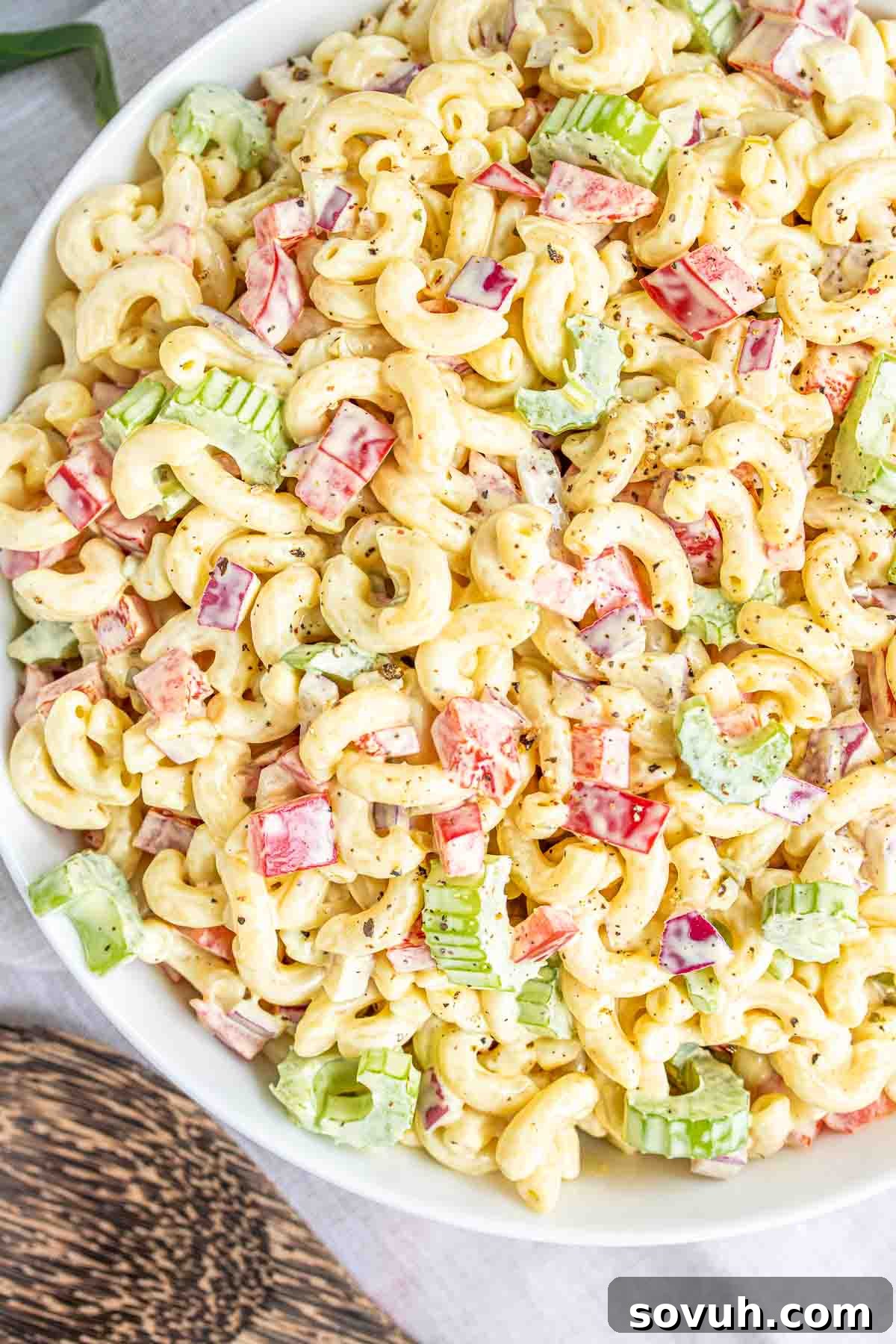 A beautiful white bowl filled with classic macaroni salad, with a wooden spoon resting inside, ready for serving at a festive gathering.