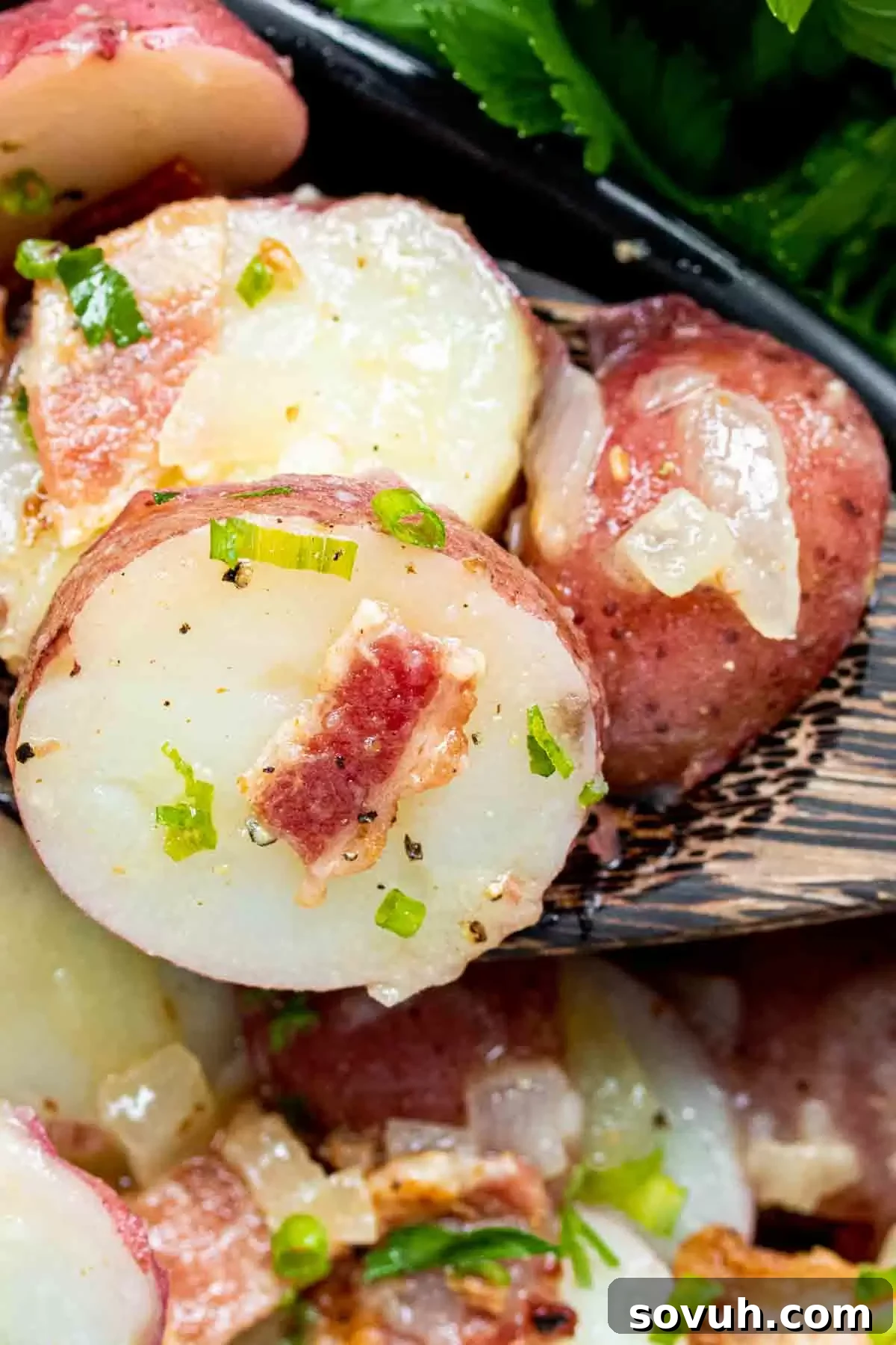 A wooden spoon carefully scooping a generous portion of warm German Potato Salad, showcasing the tender potatoes, crispy bacon, and glistening tangy dressing.