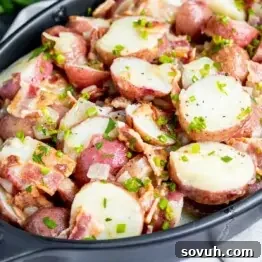 Close up of warm German Potato Salad in a black bowl, garnished with fresh herbs and bacon bits.