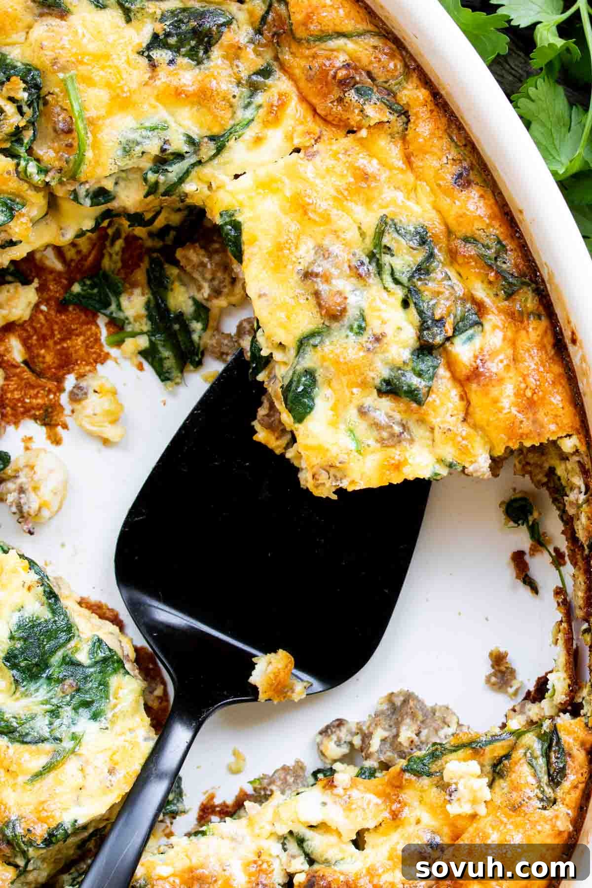 A freshly baked Sausage and Spinach Crustless Quiche with a serving utensil lifting a slice from the pan, ready to be enjoyed.