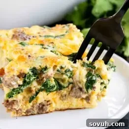 A slice of Spinach and Sausage Quiche on a plate with a fork, ready to be eaten.